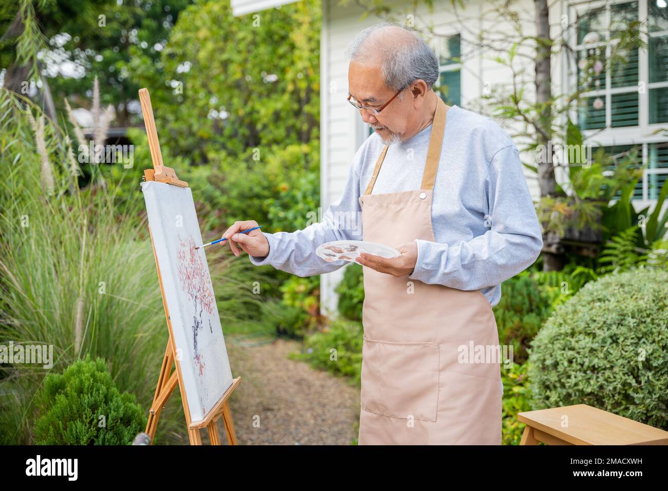 Asiatischer älterer Mann malt Bild mit Pinsel- und Ölfarbe auf Leinwand Stockfoto