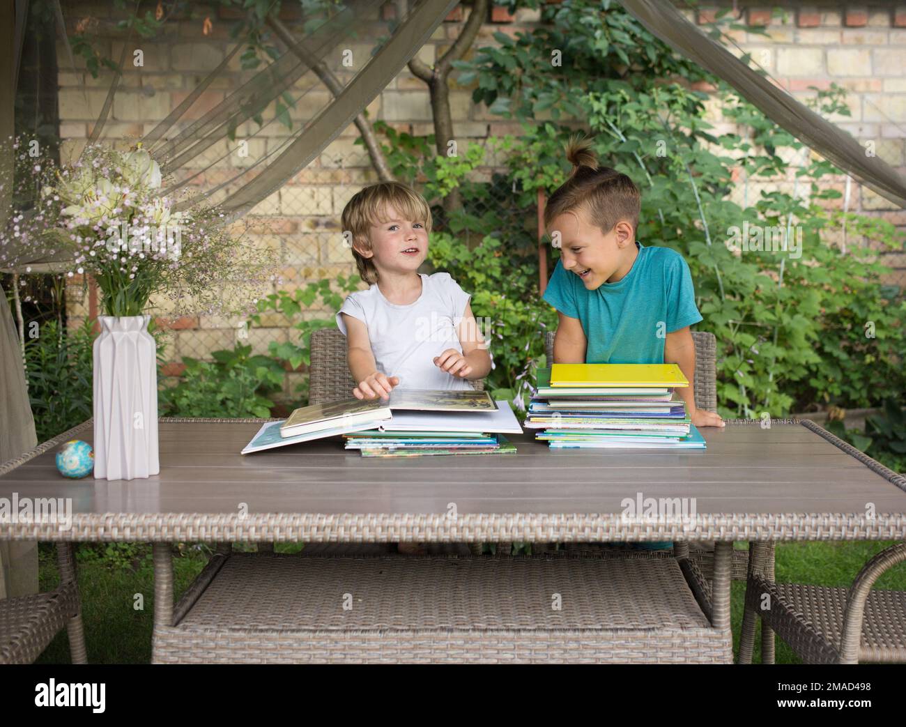 Zwei Vorschuljungen sitzen im Garten am Tisch, schauen sich Bücher an, lesen Bücher. Schulvorbereitung, Fantasieentwicklung, Kindheit, Kommunikation Stockfoto