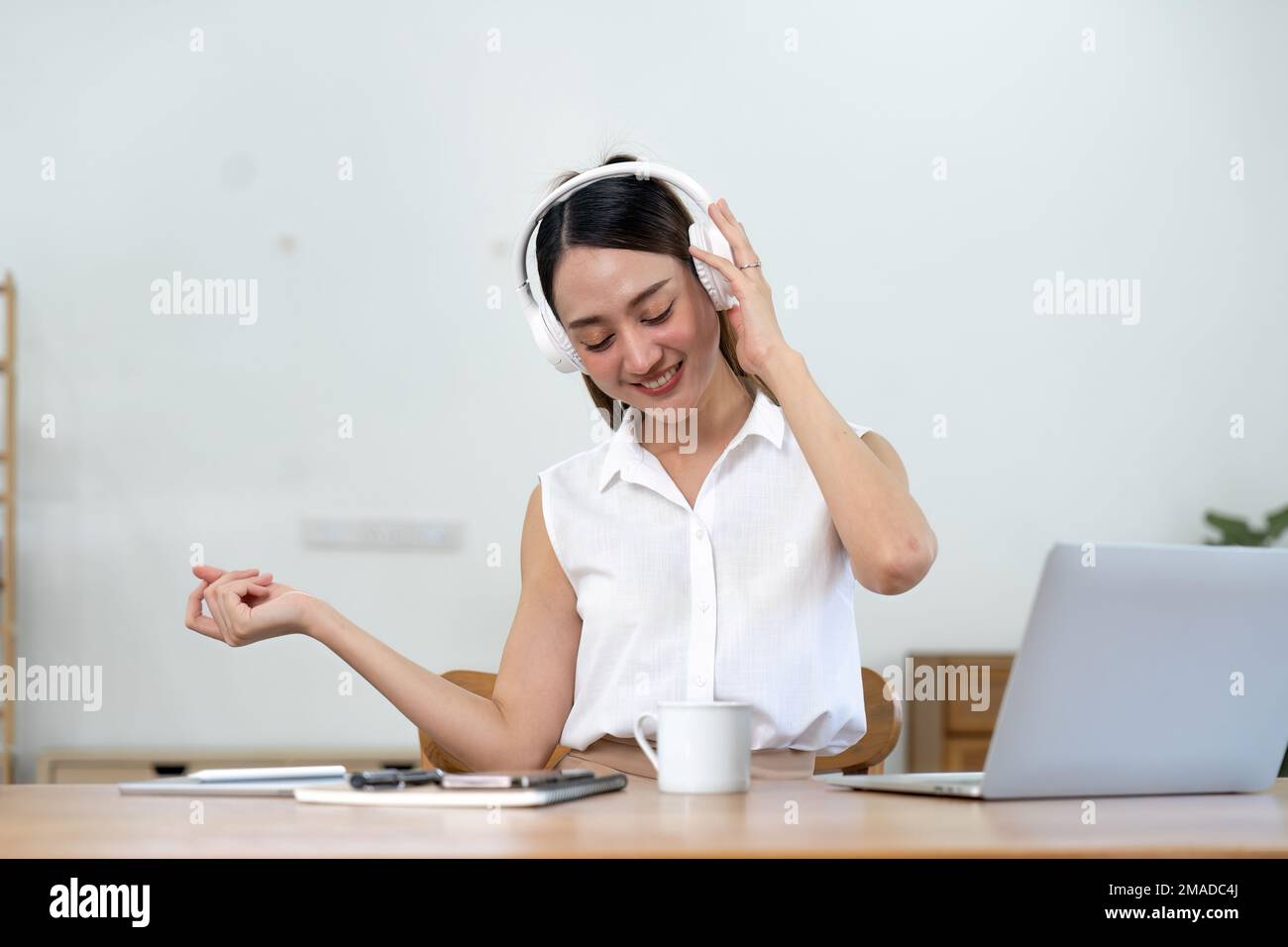 Porträt einer jungen lächelnden asiatischen Frau mit Kopfhörern, die zu Hause Musik hört Stockfoto