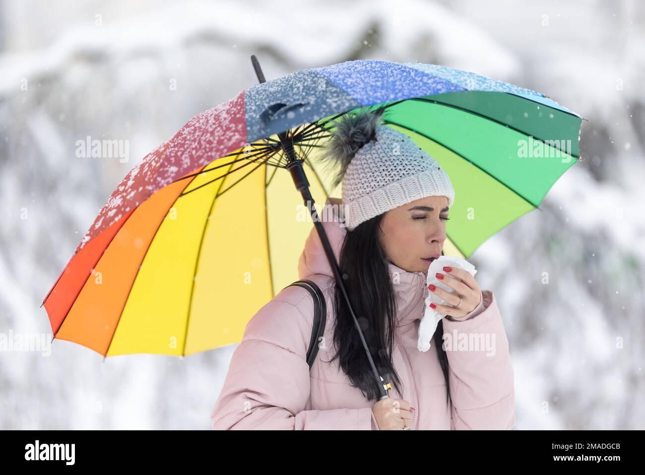 Eine Frau, die einen Schirm am kalten Regentag hält, hustet und bedeckt ihren Mund Stockfoto