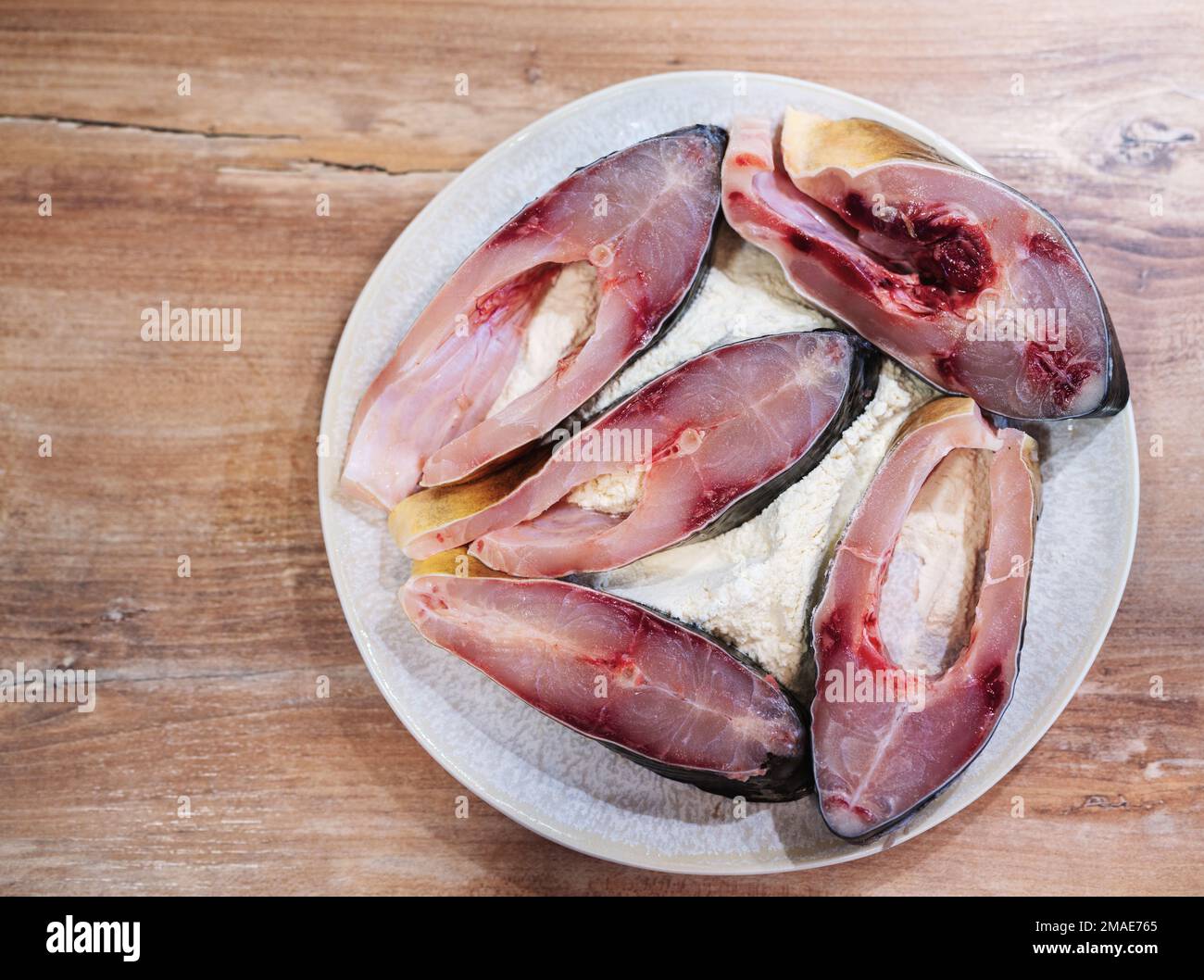 Rohe Fischsteaks auf dem Teller mit Mehl auf einem Holztisch, Karpfenfisch. Stockfoto