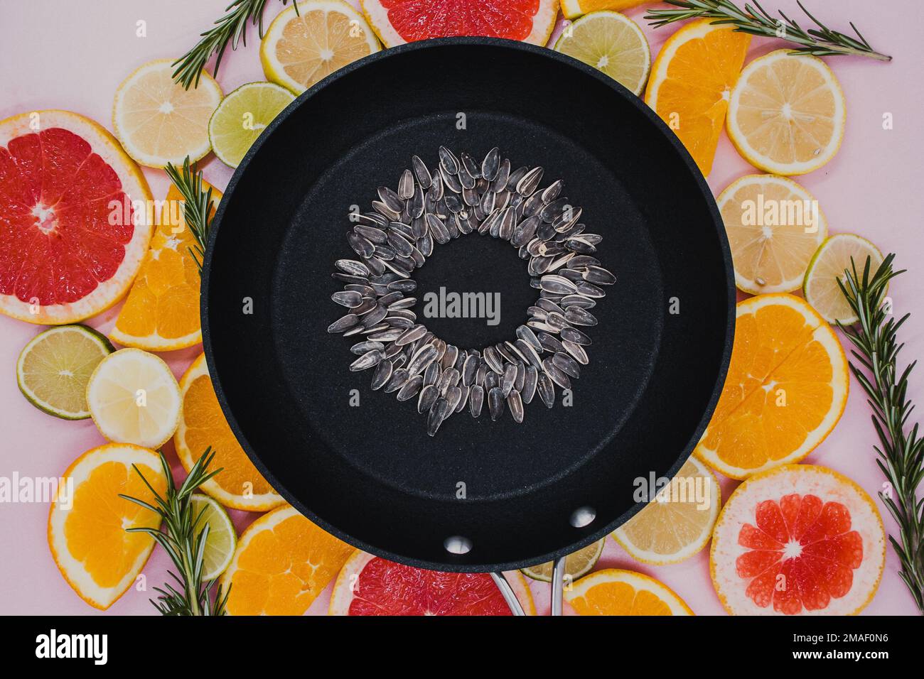 Schwarze Bratpfanne mit Sonnenblumenkernen, aus der eine Sonnenblumenblume auf in Scheiben geschnittenen Zitruspflanzen entsteht. Orangen, Grapefruit, Zitrone, Limette Stockfoto