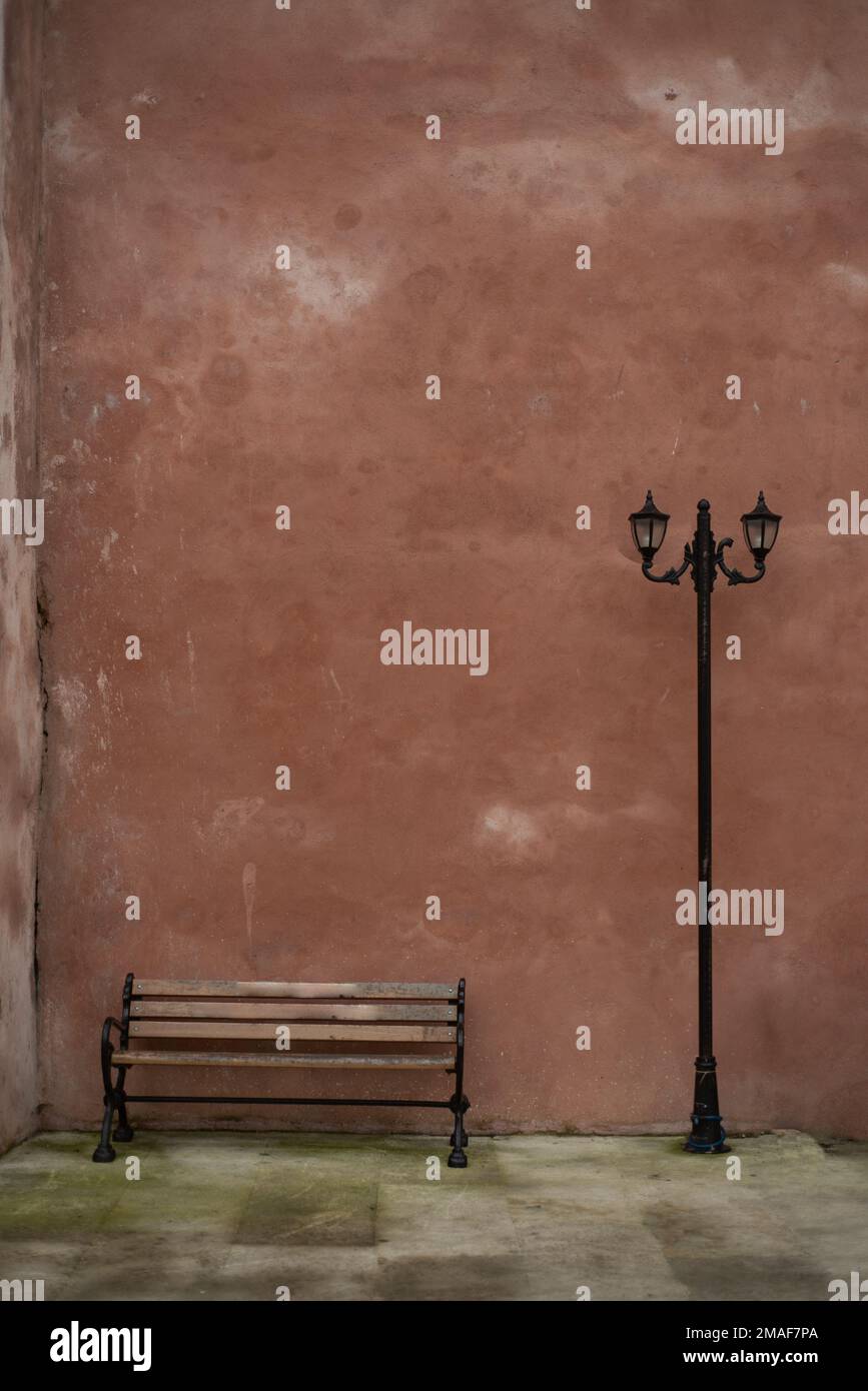 Leere Bank und Straßenlampe stehen vor der verwitterten rosafarbenen Wand, leerer Platz für Text, Retro-Hintergrund Stockfoto
