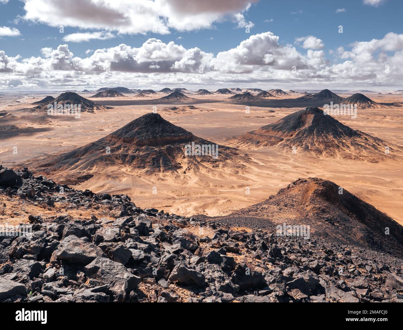 Vulkanische Hügel, Felsen und Landschaft in der Schwarzen Wüste, Ägypten an einem sonnigen und bewölkten Tag. Stockfoto