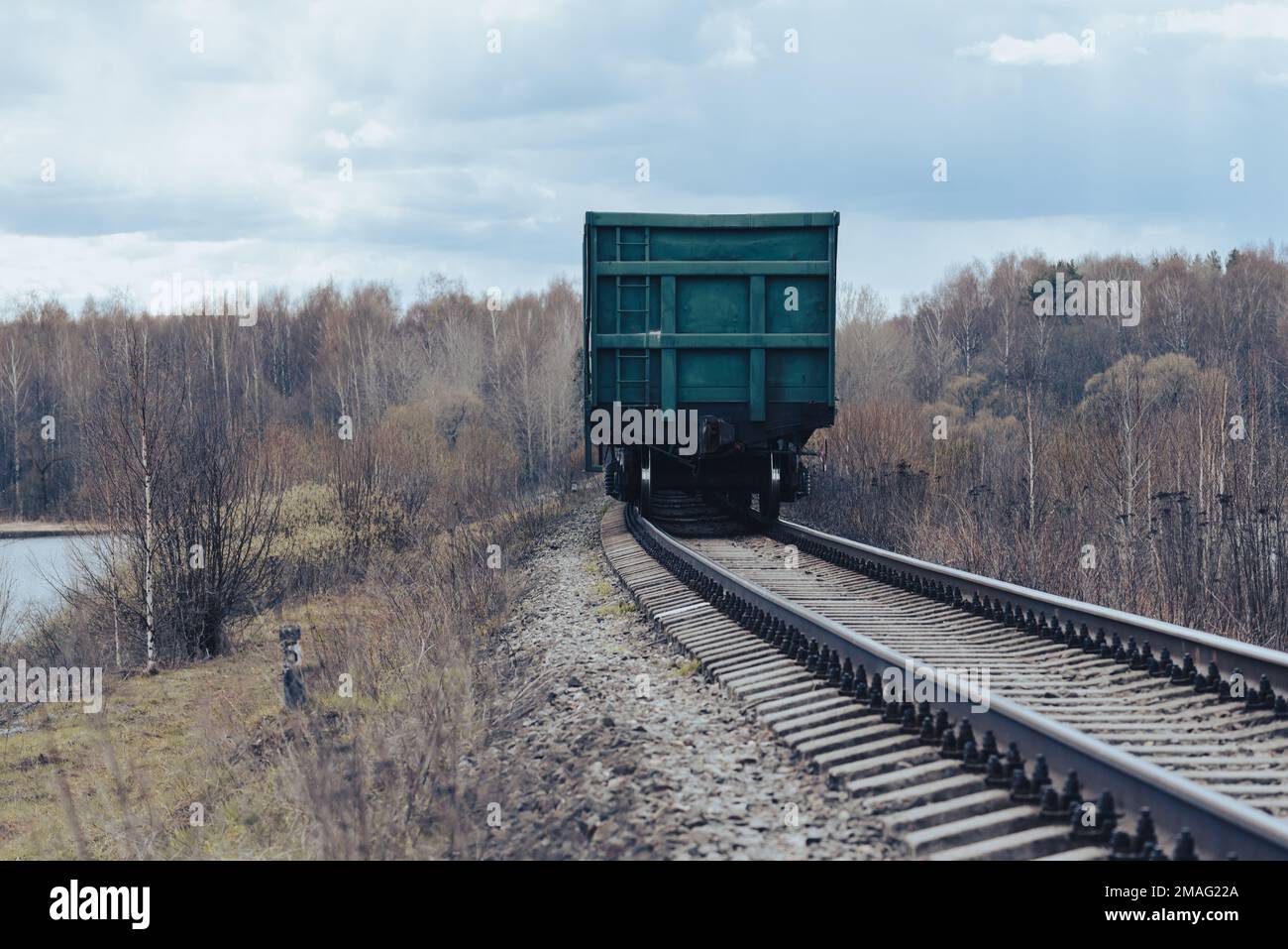 Güterzug von hinten, der durch den Winter mit der Eisenbahn wegfährt - Frühlingslandschaft. Zugwaggon für Getreidetransport Stockfoto