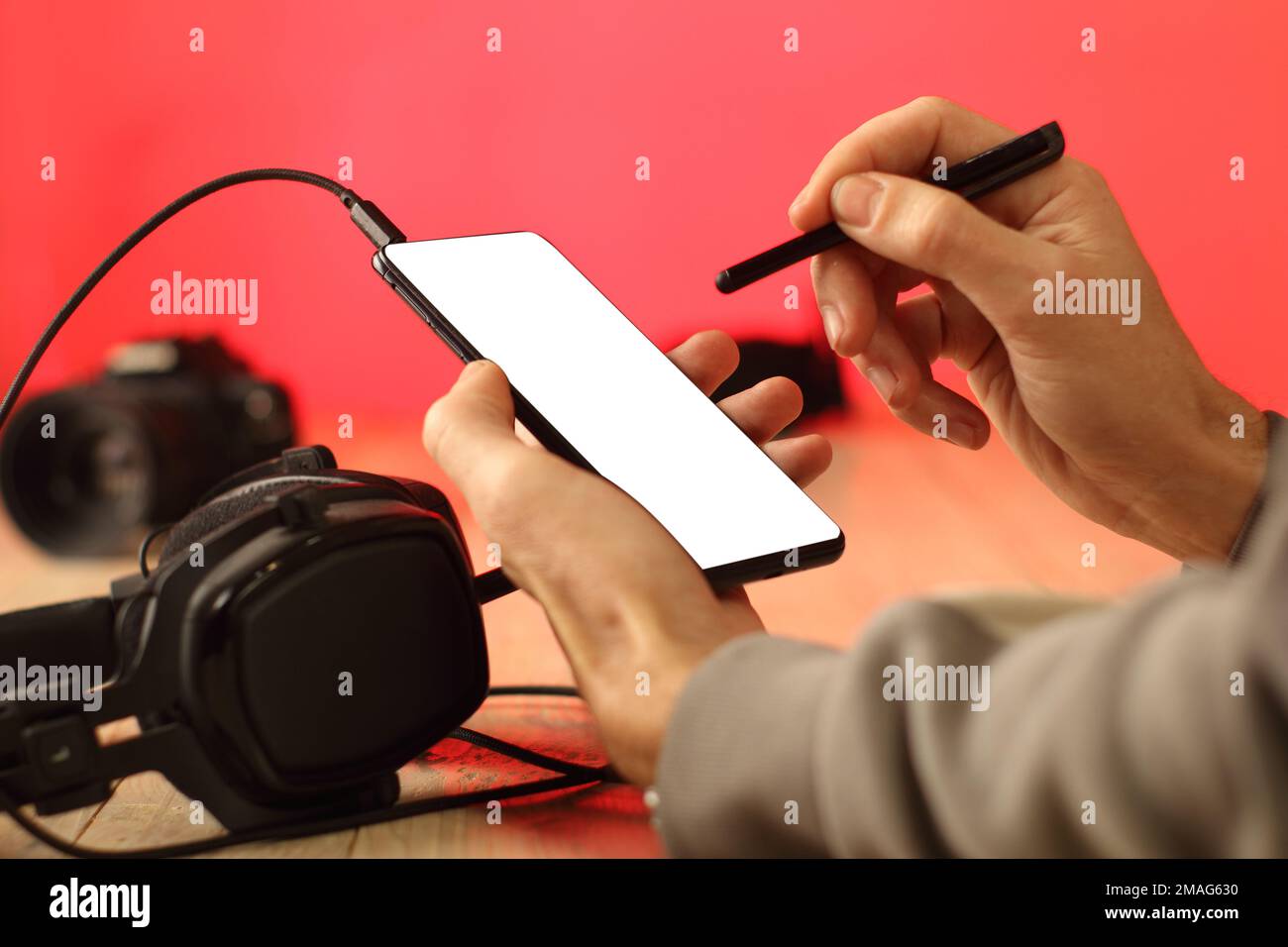 Eine Person, die mit einem Eingabestift auf einem Smartphone vor dem Hintergrund von Kopfhörern und einer farbigen Wand schreibt Stockfoto