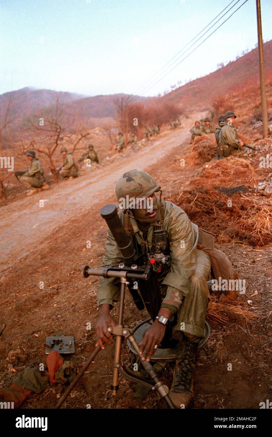 Ein Soldat der 1. Milliarden, 14. Inf., 25. Inf. Div. Baut einen M-224 60mm-Mörser zusammen, während andere Soldaten während der gemeinsamen US/Südkoreanischer Übungstruppe Spirit '86 Deckung an einer Straße suchen. Operation/Serie: MANNSCHAFTSGEIST '86 Basis: Mandeul Land: Südkorea Stockfoto