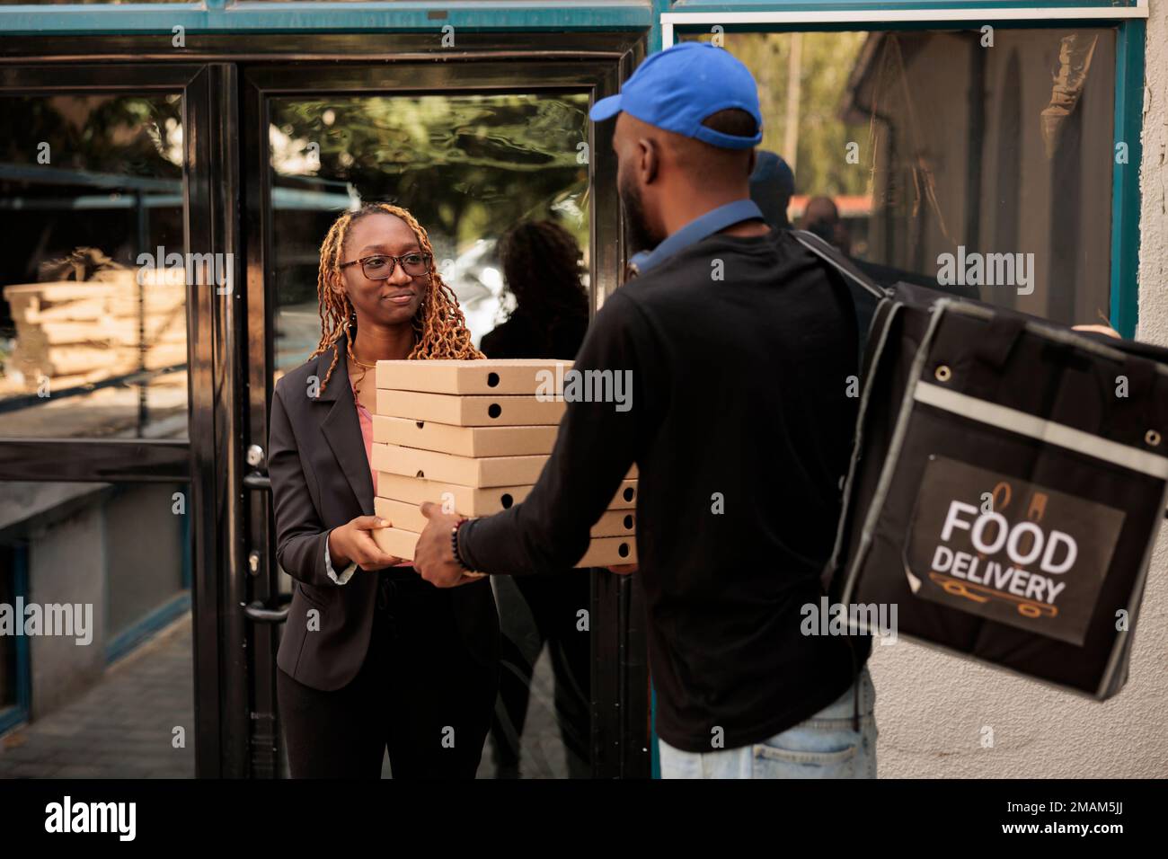 Pizzalieferung ins Büro, lächelnde Kunden, die Kartons stapeln, Bestellungen vom Kurier im Freien erhalten. afroamerikanischer Angestellter nimmt Essenspakete auf, Mann liefert Mittagessen Stockfoto