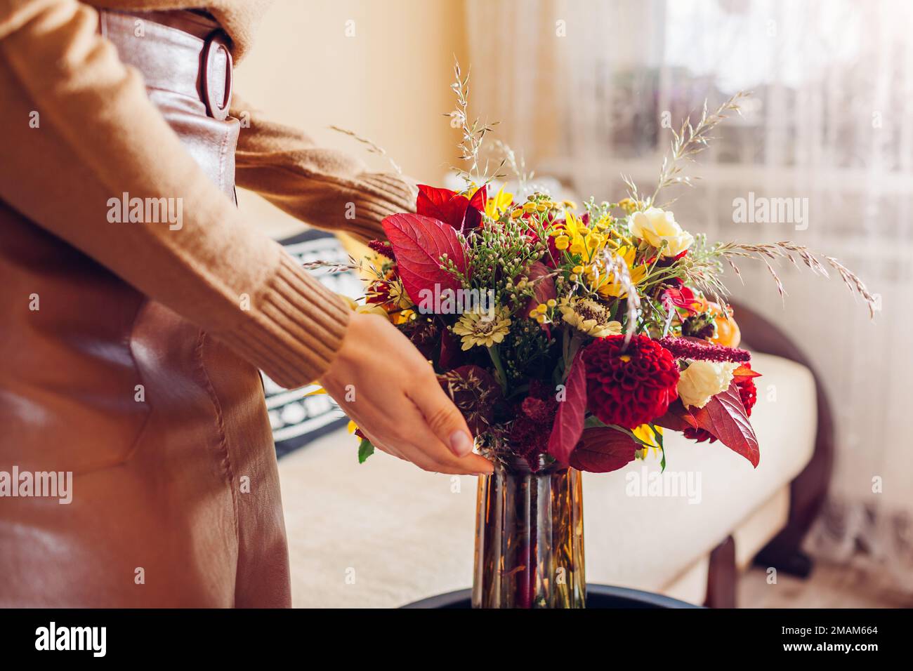 Frau stellt Vase mit Blumenstrauß von Sonnenblumen Dahlien Rosen und Zinnia Blumen auf den Tisch. Innenausstattung und Herbstdekor zu Hause. Stockfoto
