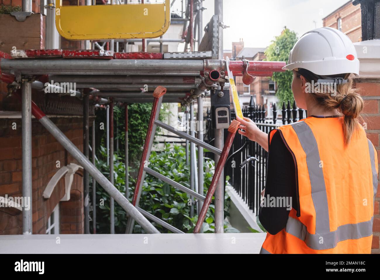 Eine Ingenieurin, die eine Inspektion durchführt und ein Baustellengebäude überwacht, trägt einen Schutzhelm und eine orangefarbene PSA Stockfoto