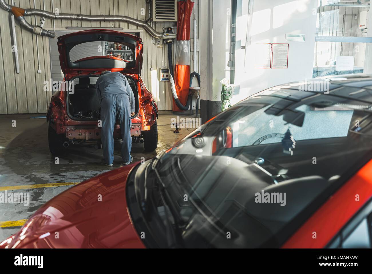 Erfahrener Mechaniker diagnostiziert und repariert ein rotes Auto in einer geschäftigen Autowerkstatt. Hochwertige Fotos Stockfoto