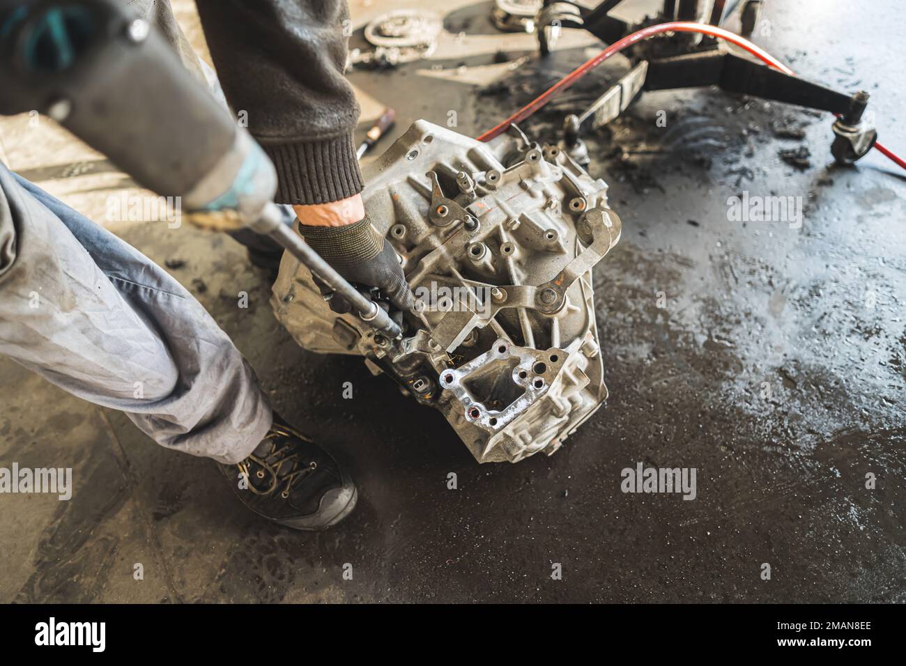 Mechaniker mit Handschuhen ersetzt die Kupplungsscheibe des Getriebes im Fahrzeug an der Tankstelle. Hochwertiges Foto Stockfoto