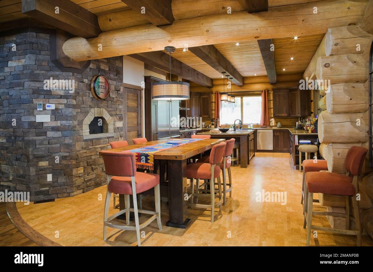 Wiederaufbereitete Scheune Holztisch mit orangen Stoff gepolsterte Hochstühle und Naturstein Pizzaofen in der Küche in luxuriösem skandinavischem Blockhaus. Stockfoto