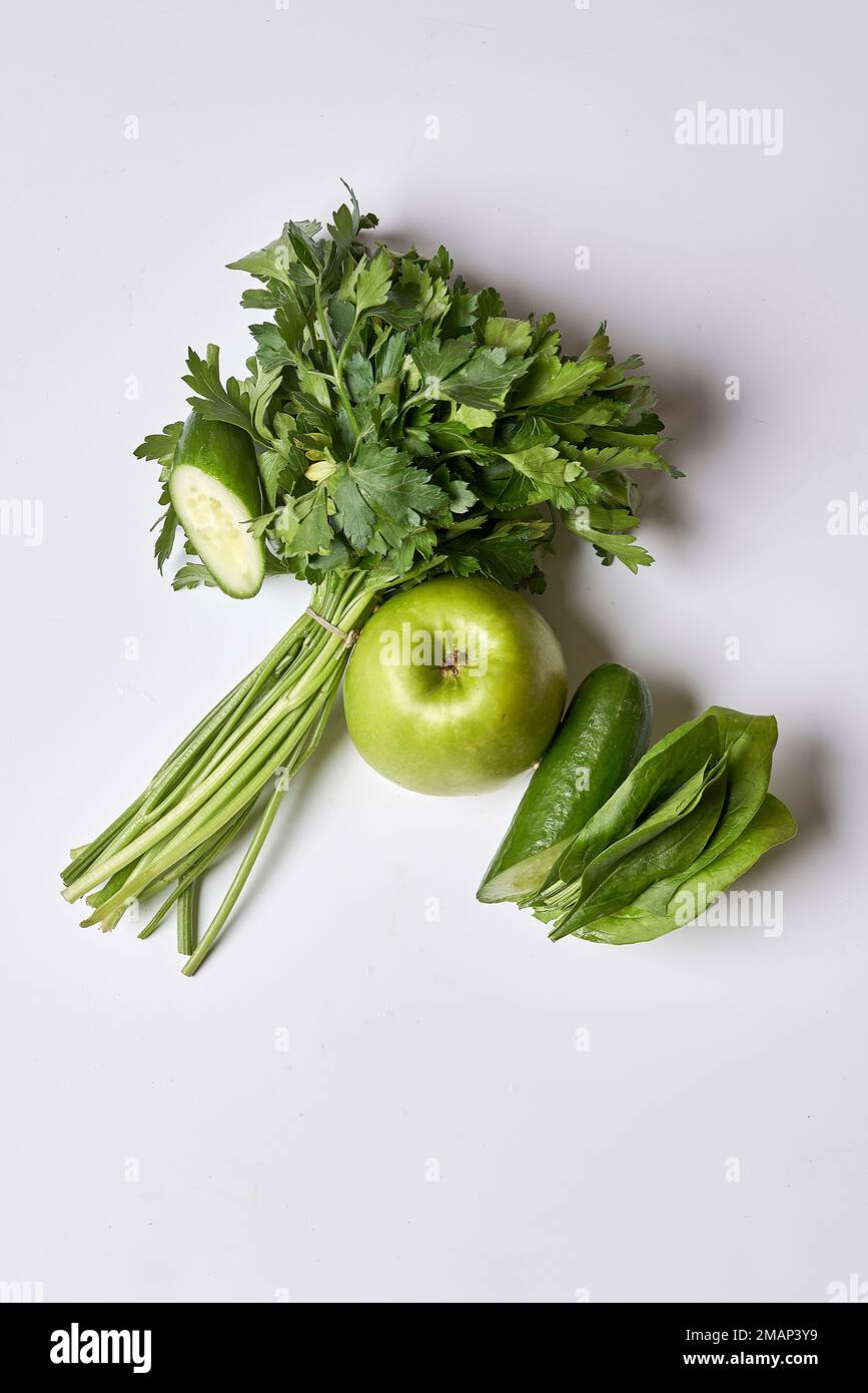 Etwas grünes Gemüse auf einer weißen Oberfläche mit einem Apfel und den anderen zwei Apfelspuren im Hintergrund Stockfoto