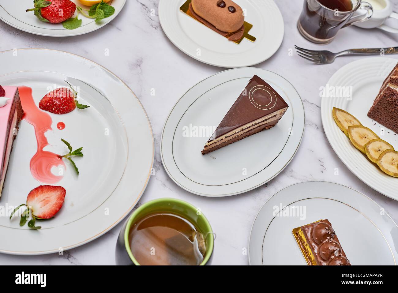 Einige Desserts auf Tellern mit Tassen und Löffeln nebeneinander an der gleichen Stelle Stockfoto