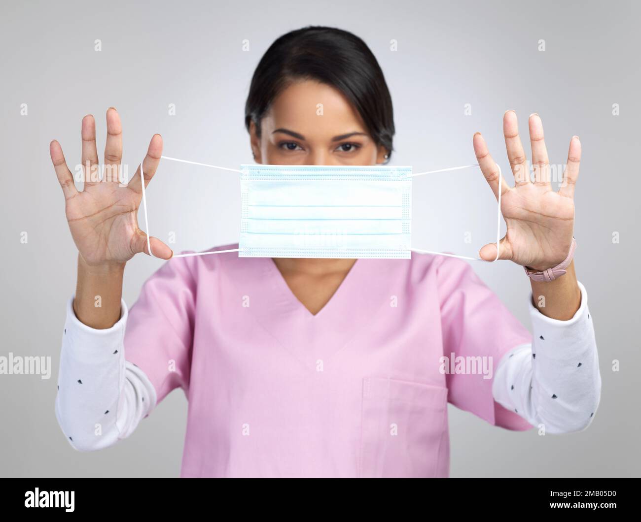 Zeit zum Abwickeln der Kurve. Gekürztes Porträt einer attraktiven jungen Gesundheitsarbeiterin, die eine Maske im Studio vor einem grauen Hintergrund hochhält. Stockfoto