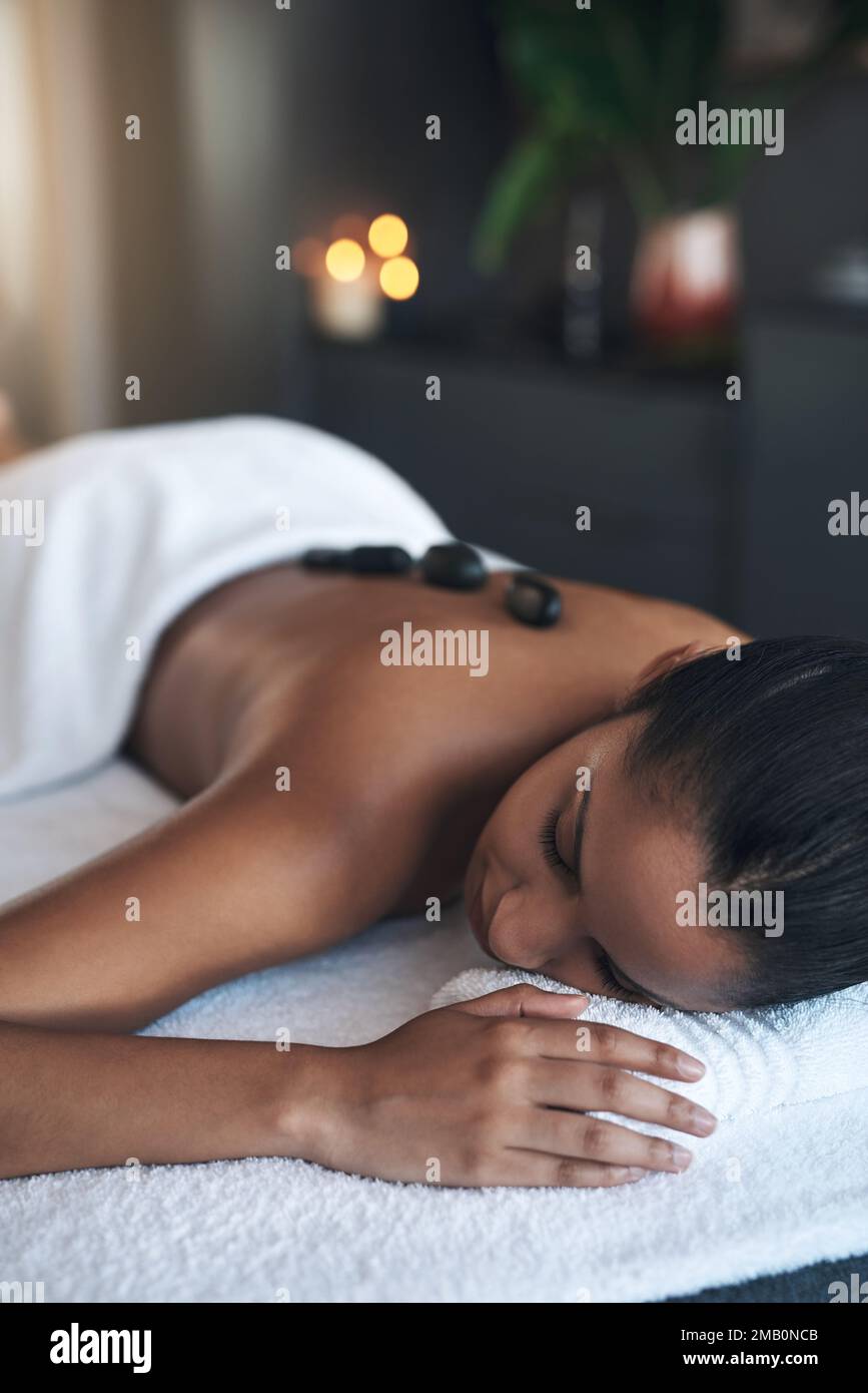 Legen Sie sich hin und nehmen Sie die ganze ruhige Energie auf. Eine junge Frau, die eine Hot-Stone-Massage in einem Spa bekommt. Stockfoto
