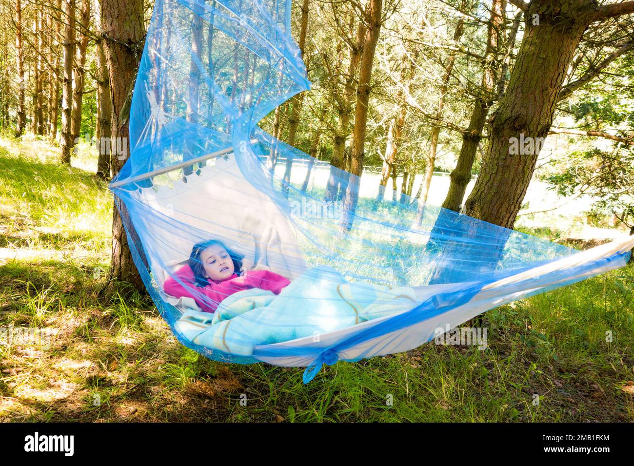 Ein Mädchen, das sich an einem sonnigen Tag in einer Hängematte mit Moskitonetz im Wald entspannt. Stockfoto