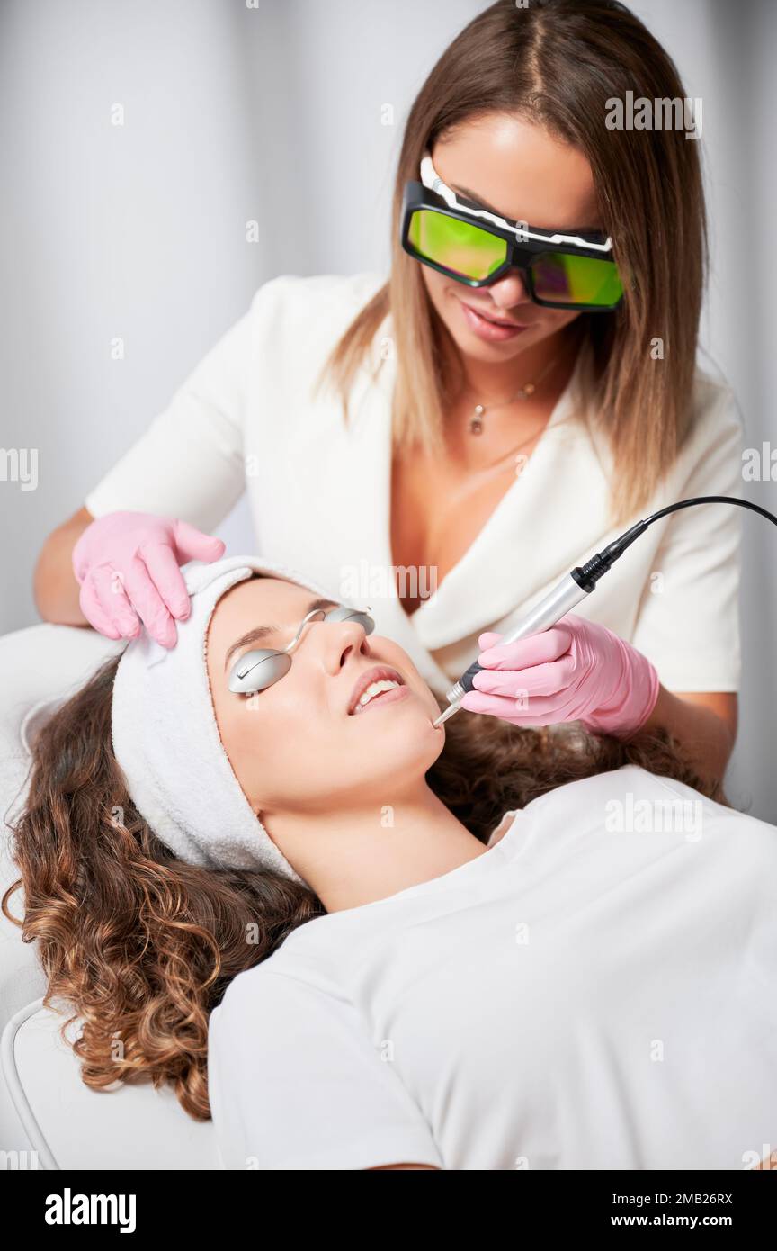 Augenschutzpatientin bei Laserbehandlung von Gesichtsgefässen im Schönheitssalon. Weibliche Kosmetikerin entfernt Teleangiektasien schmerzlos und schnell aus dem Gesicht. Stockfoto