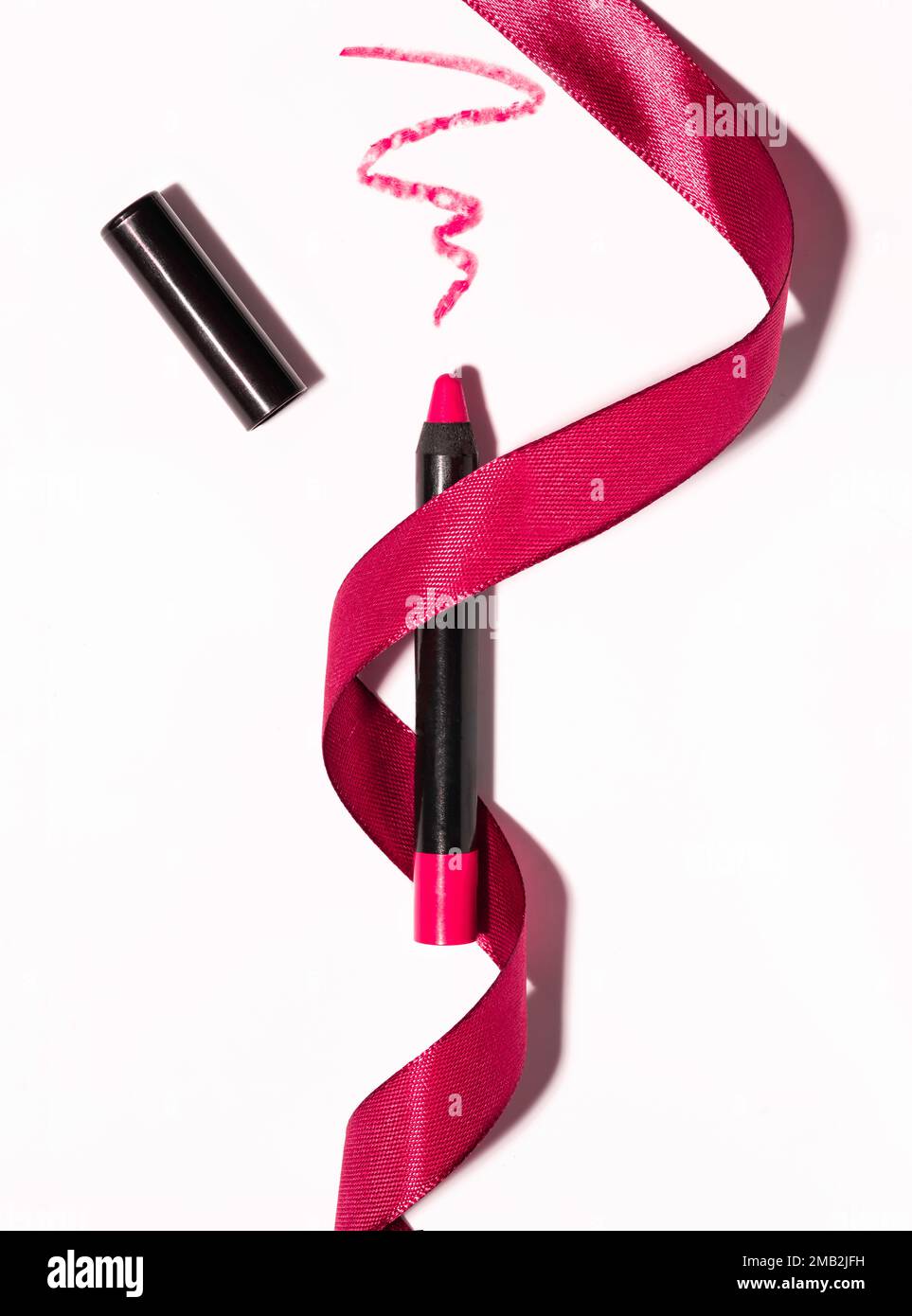 Roter matter Lippenstift in Form eines Bleistifts mit rotem Band, schmierter Textur auf weißem Hintergrund Stockfoto