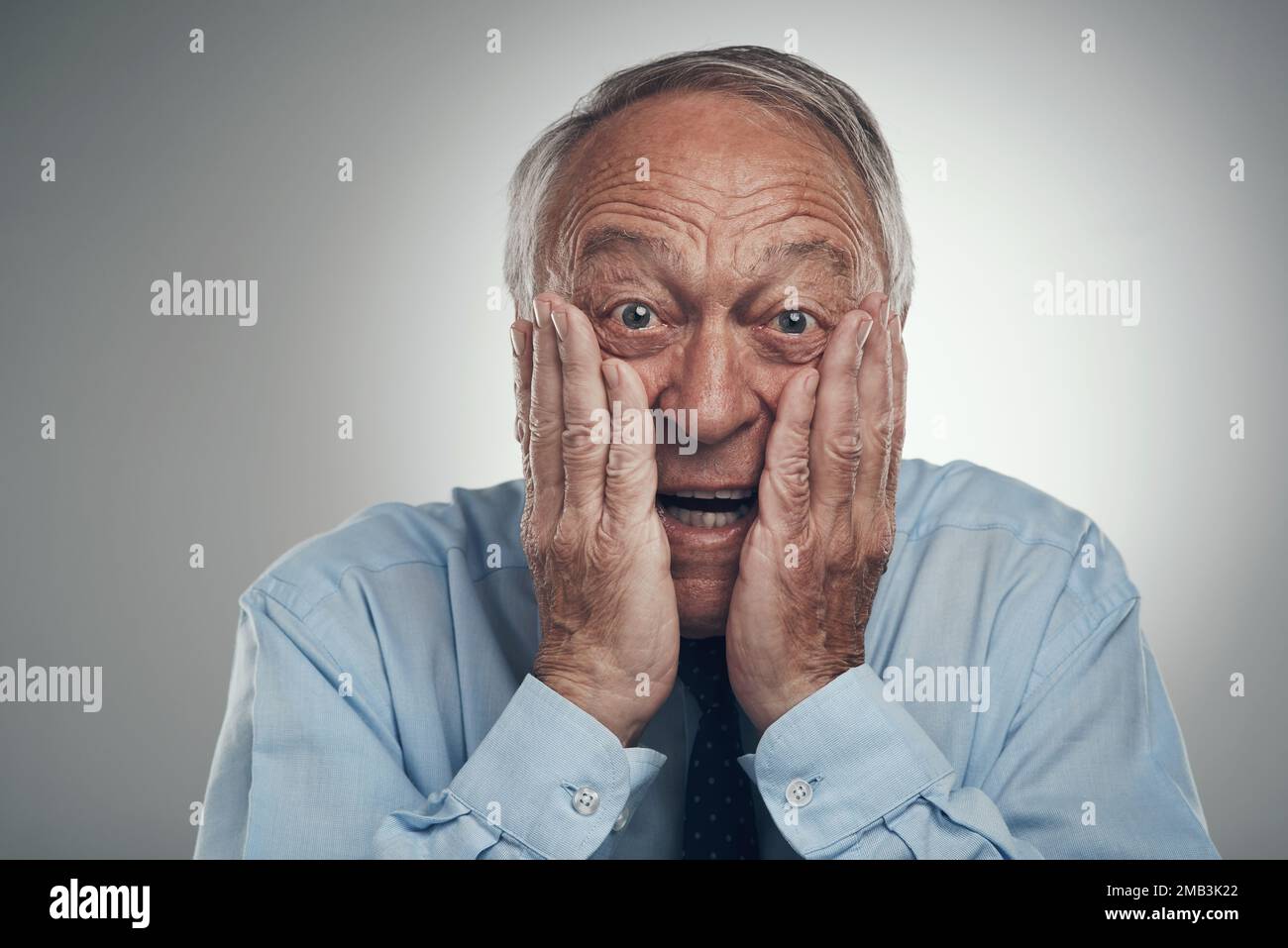 Hast du gesehen, was ich gesehen habe? Ein Geschäftsmann, der vor einem grauen Studiohintergrund steht, sein Gesicht in den Händen hat und überrascht aussieht. Stockfoto