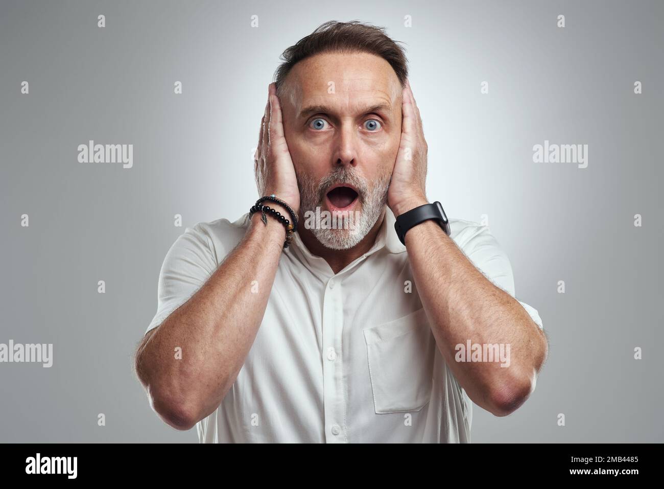 Ich will es nicht hören. Studioporträt eines erwachsenen Mannes, der sich die Ohren zudeckt und vor grauem Hintergrund schockiert aussieht. Stockfoto