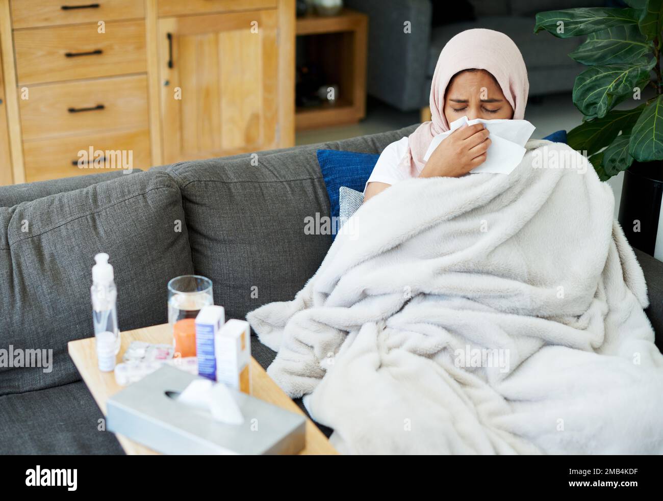 Kann diese Grippe Geh weg. gefallen Eine attraktive junge Frau, die allein auf ihrem Sofa zu Hause sitzt und sich krank fühlt. Stockfoto