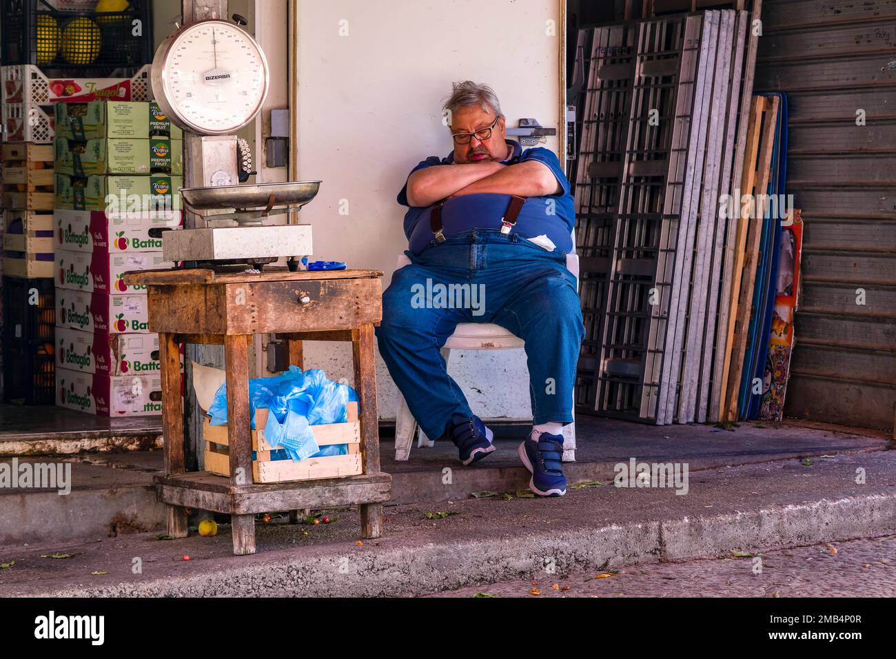 Ein Verkäufer macht vor seinem Laden ein Nickerchen auf dem lokalen Ballaro Markt. Stockfoto