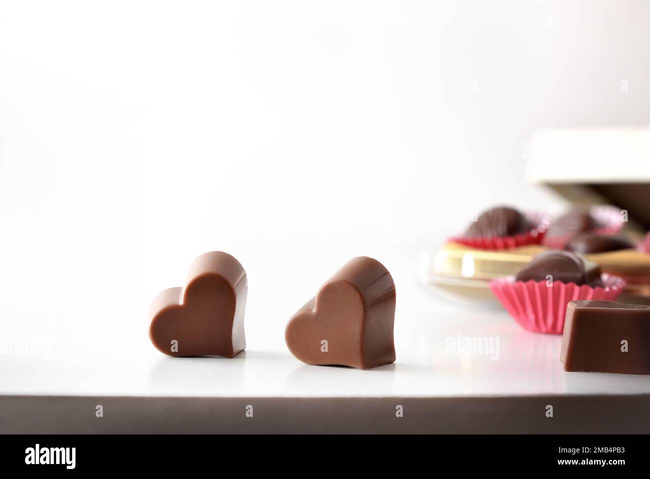 Herzförmige Schokolade auf weißem Tisch und Schachtel Pralinen auf weißem, isoliertem Hintergrund. Vorderansicht. Stockfoto