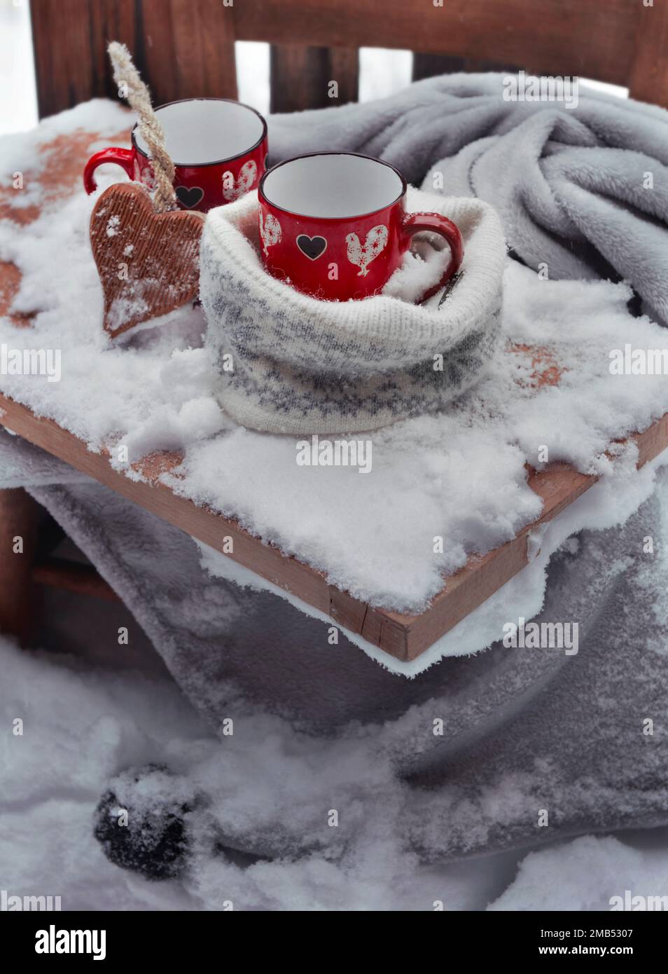 Zwei rote Tassen mit Herzform auf einer Planke, die auf einem karierten Schneefall auf der Terrasse platziert wird Stockfoto