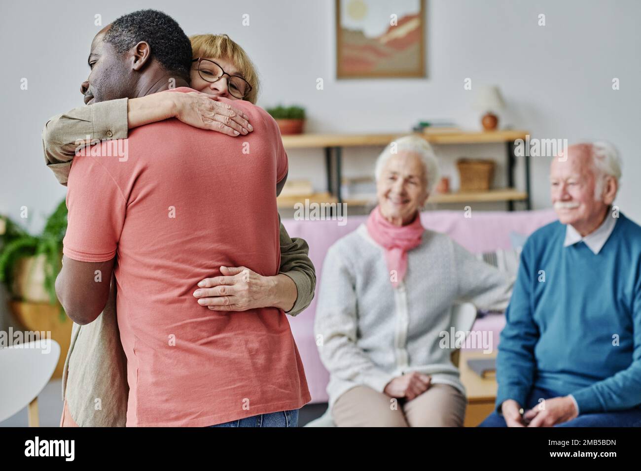 Die Senioren freuten sich, sich zu sehen, sie stehen im Raum und umarmen sich Stockfoto
