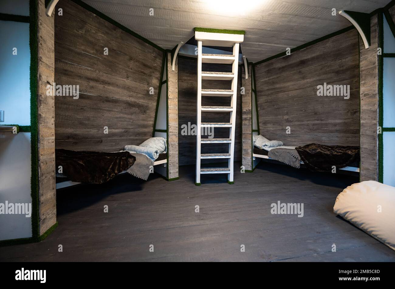 Zwei Einzelbetten mit Bettwäsche in Nischen eines Zimmers. Pyramidenförmiges Bungalow Sommerhaus. Abgewinkelte umgebene Wände, weiße Treppen, grauer horizontaler Arbeitsplatz Stockfoto