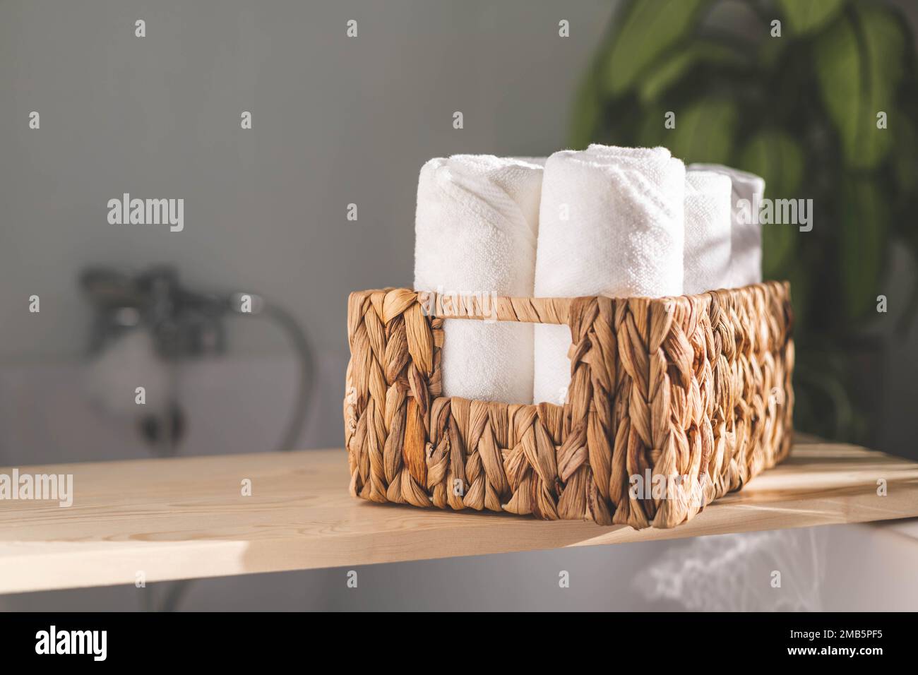 Weiße Badetücher, gerollt in einem Jutekorb auf einem Holzregal, Stauraum im Badezimmer Stockfoto