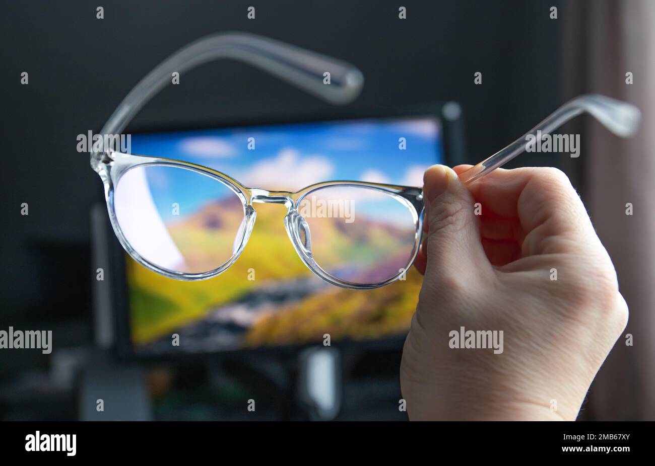 Selektiver Fokus auf transparente, klare, blaue Computerbrillen und einen Computerbildschirm, der im Hintergrund zu Hause oder im Büro leuchtet. Blaue Lichtbrille. Stockfoto