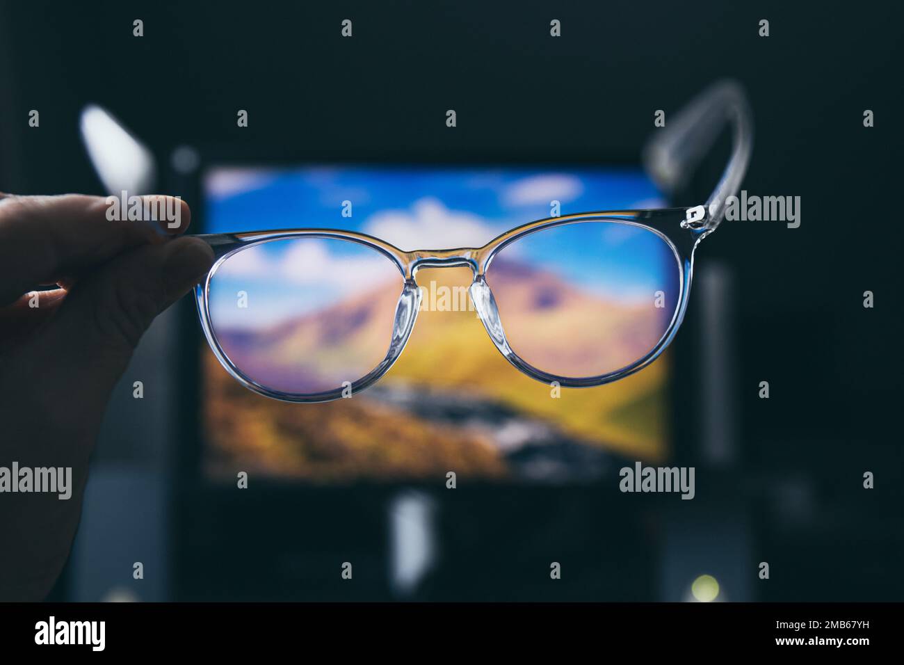 Selektiver Fokus auf transparente, klare, blaue Computerbrillen und einen Computerbildschirm, der im Hintergrund zu Hause oder im Büro leuchtet. Blaue Lichtbrille. Stockfoto