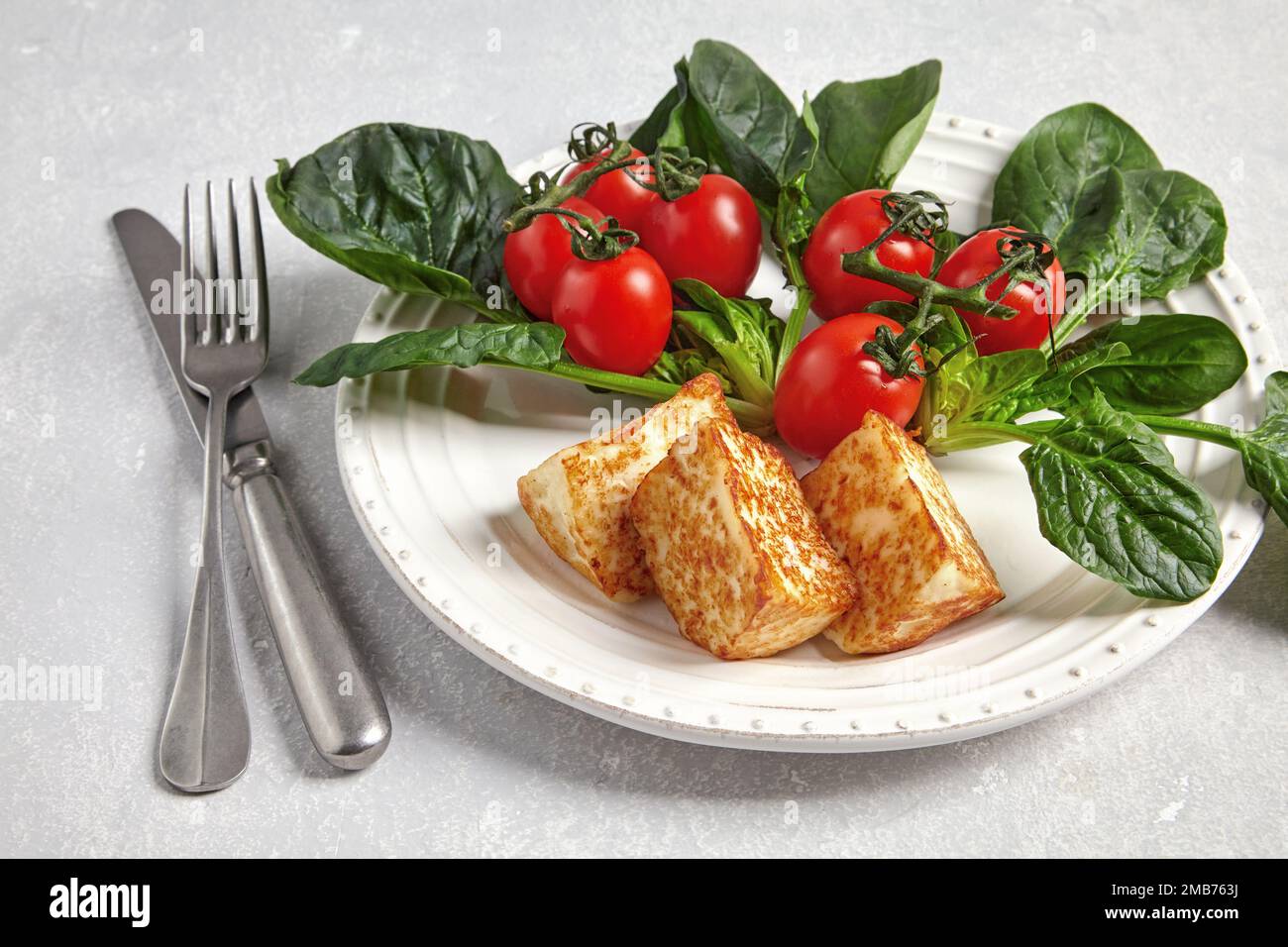 Gebratener Quark Mozzarella halloumi mit grünem Spinat und Kirschtomaten auf einem Zweig mit Besteck Stockfoto