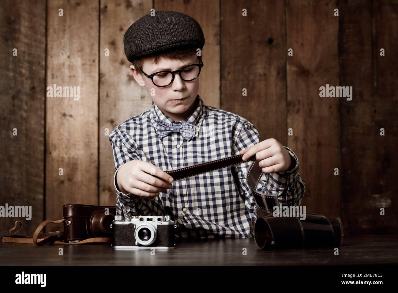 Die werden sich gut entwickeln. Ein Junge in Retro-Kleidung, der eine Brille trägt und ein fotografisches Negativ überprüft. Stockfoto