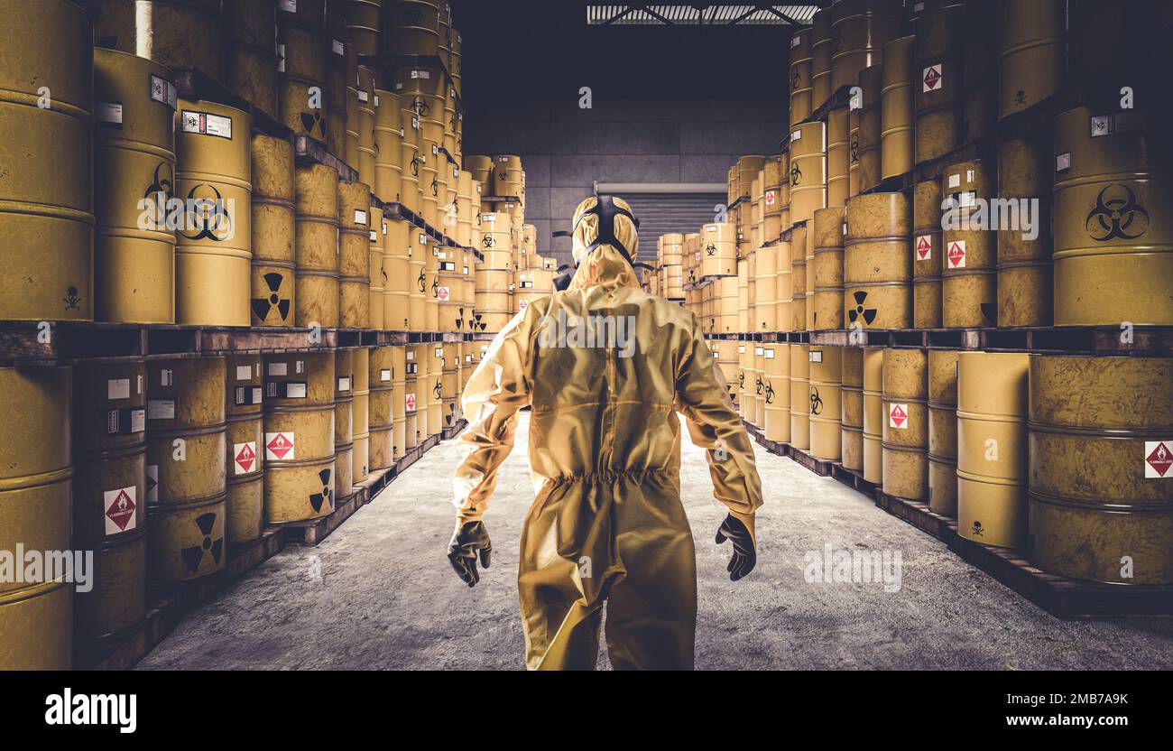 Mann in gelbem Schutzanzug und Gasmaske, Lagerhaus voller gelber Metallfässer mit Gefahrensymbolen. Stockfoto