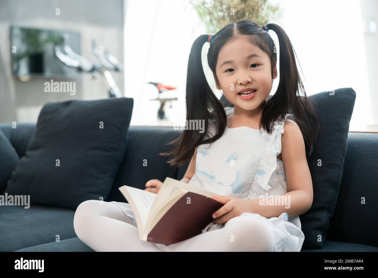 Das kleine Mädchen auf dem Sofa, das ein Buch liest Stockfoto