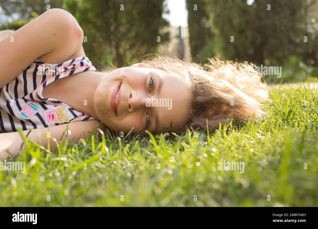Porträt eines lächelnden Teenagers von 12 Jahren, das an einem sonnigen Tag auf dem Gras liegt. Natur an der frischen Luft genießen, Entspannung, Träume. Fröhlicher Sommer Stockfoto