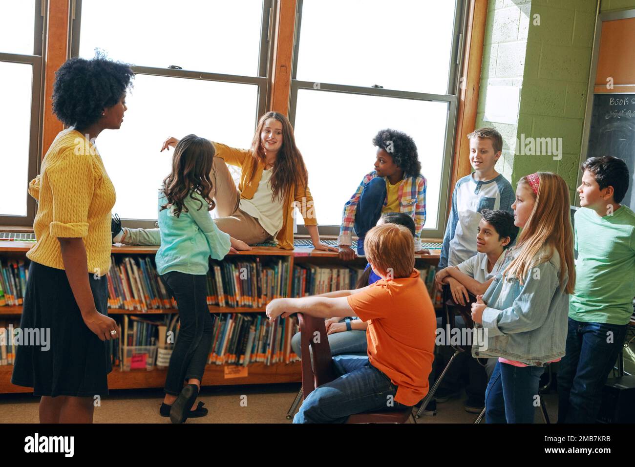 Bildungsbibliothek, Lehrer und Schüler im Klassenzimmer der Grundschule. Entwicklung, Lernstipendium und eine Gruppe von Kindern, die sich unterhalten Stockfoto