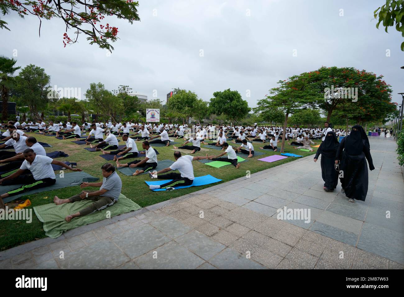 Muslim women walk past as Rapid Action Force personals and their family members perform Yoga at a garden ahead of International Yoga Day in Ahmedabad, India, Monday, June 20, 2022. (AP Photo/Ajit Solanki) Stockfoto