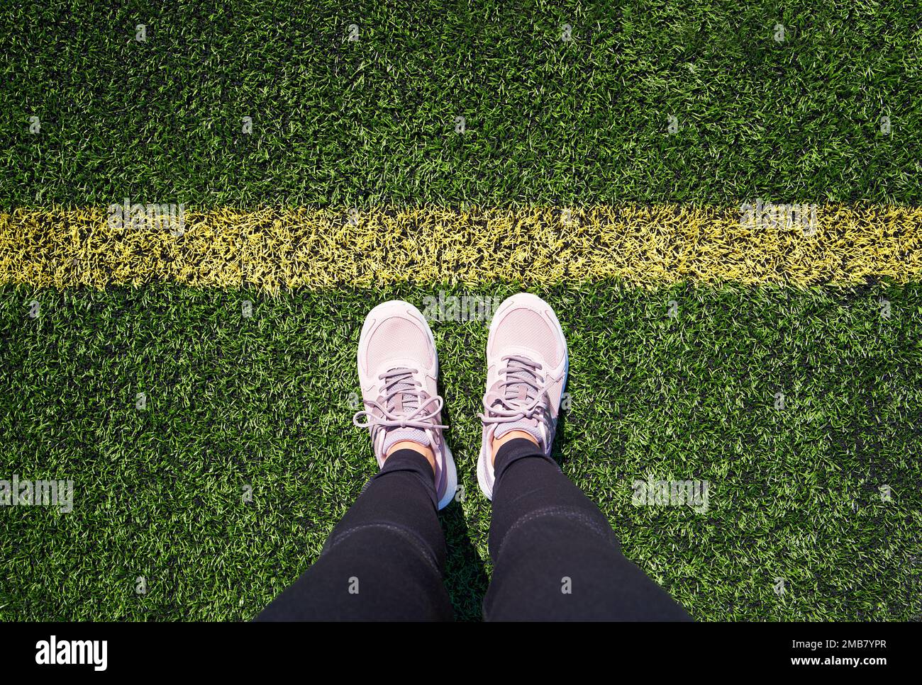 Beine einer Frau, die auf einem grünen Sportplatz vor einer gelben Linie steht, Draufsicht Stockfoto
