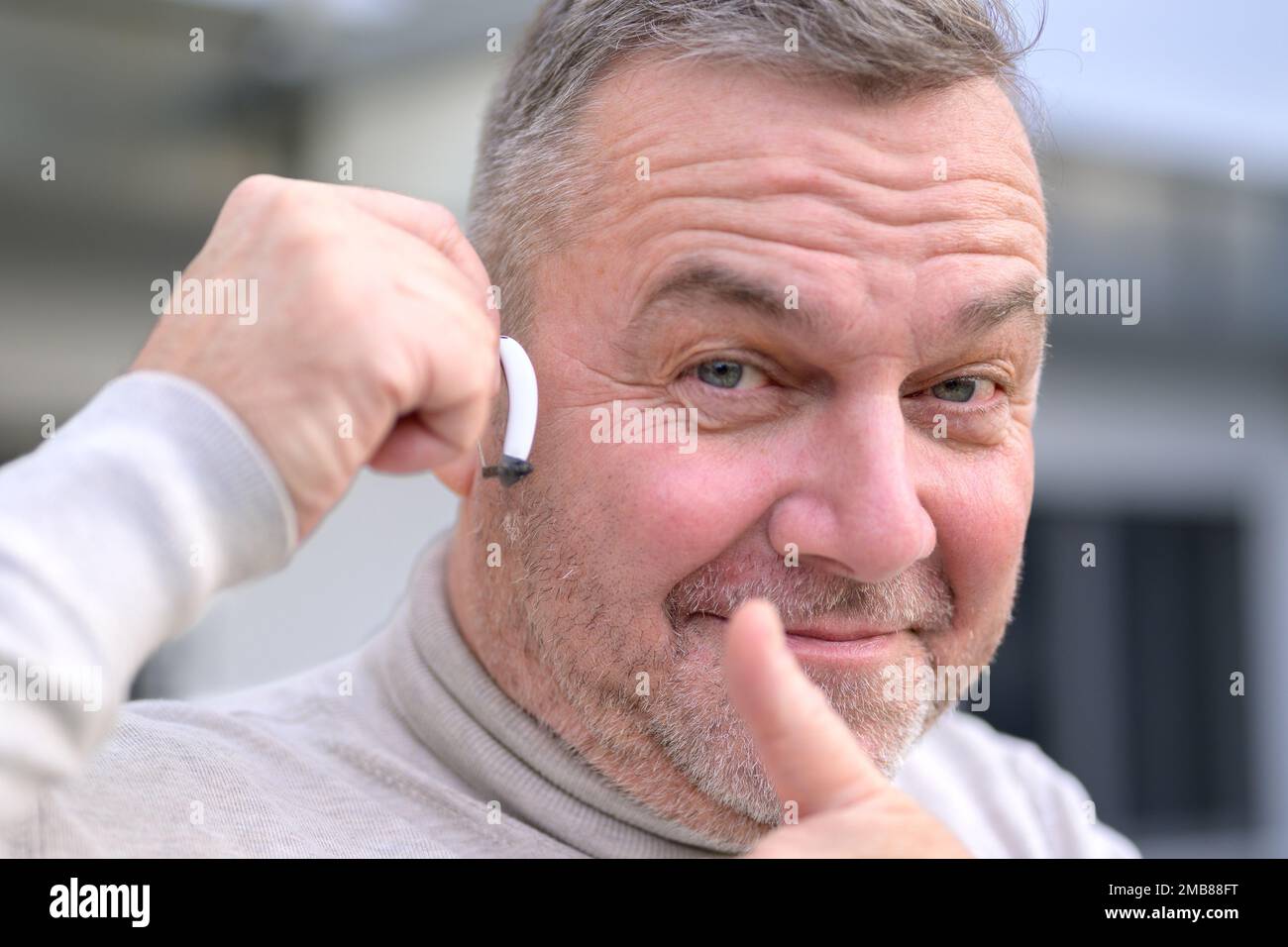 Porträt eines grauhaarigen Schwerhörigen mittleren Alters zwischen 50 und 60 Jahren mit einem Hörgerät im Ohr, das Daumen nach oben gibt Stockfoto