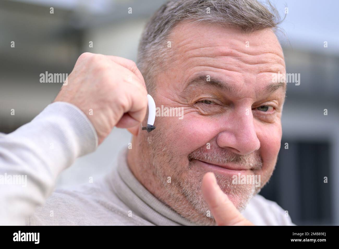 Porträt eines grauhaarigen Schwerhörigen mittleren Alters zwischen 50 und 60 Jahren mit einem Hörgerät im Ohr, das Daumen nach oben gibt Stockfoto