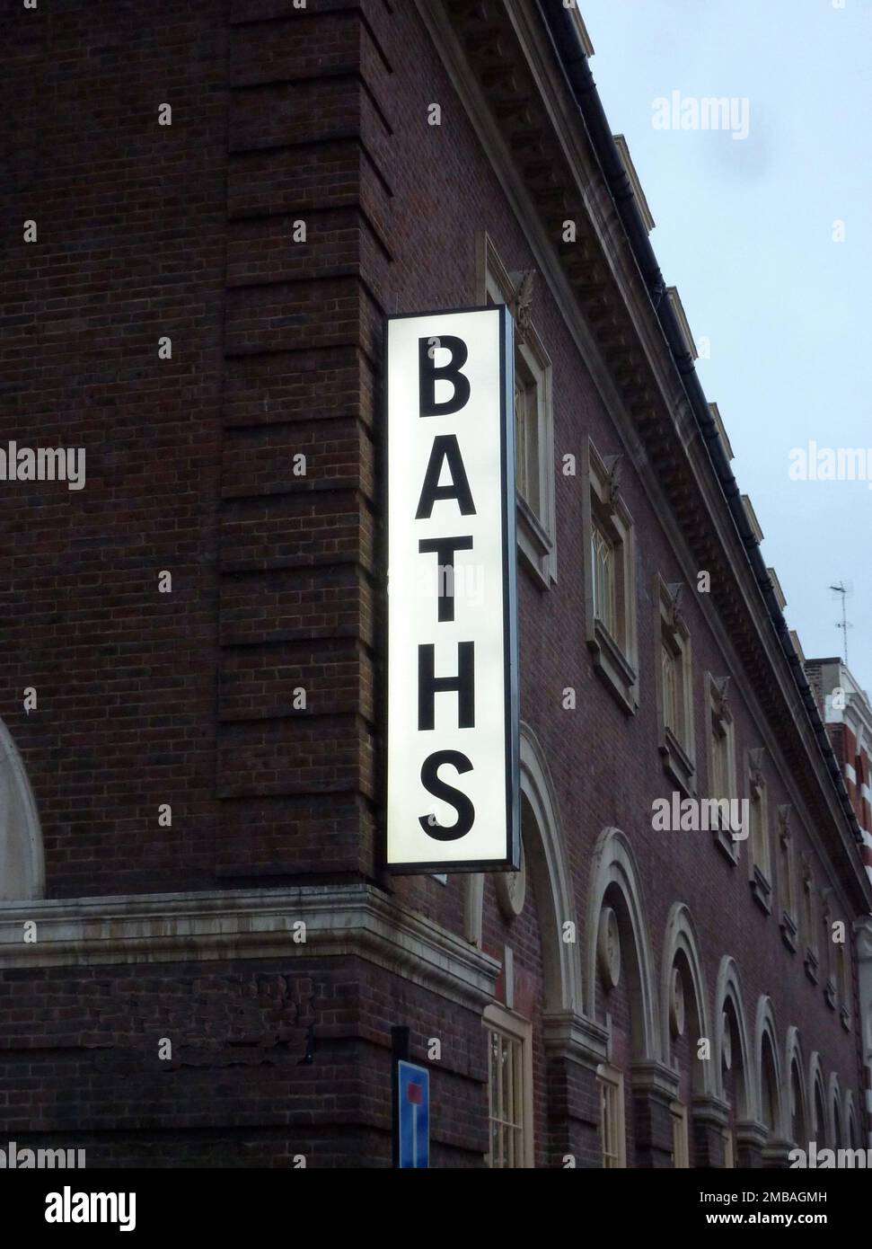 Eisonmonger Row Baths, Ironmonger Row, St. Luke's, Islington, Greater London Authority, 2013. Das beleuchtete vertikale Schild mit der Aufschrift "Baths" an der Ecke Ironmonger Row und Norman Street der Ironmonger Row Baths, Islington. Die Bäder wurden in zwei Phasen vom Gemeinderat Finsbury gebaut. Die erste Phase, die von Alfred William Stephens Cross und Kenneth Mervyn Baskerville Cross entworfen und 1931 abgeschlossen wurde, bestand aus einer Wäscherei und einem Hausschuhbad. Die zweite Phase, entworfen von K M B Cross, wurde 1938 eröffnet und umfasste den Hauptpool, das Kinderbecken und das türkische Bad. Trotz Renovierungsarbeiten im Stockfoto