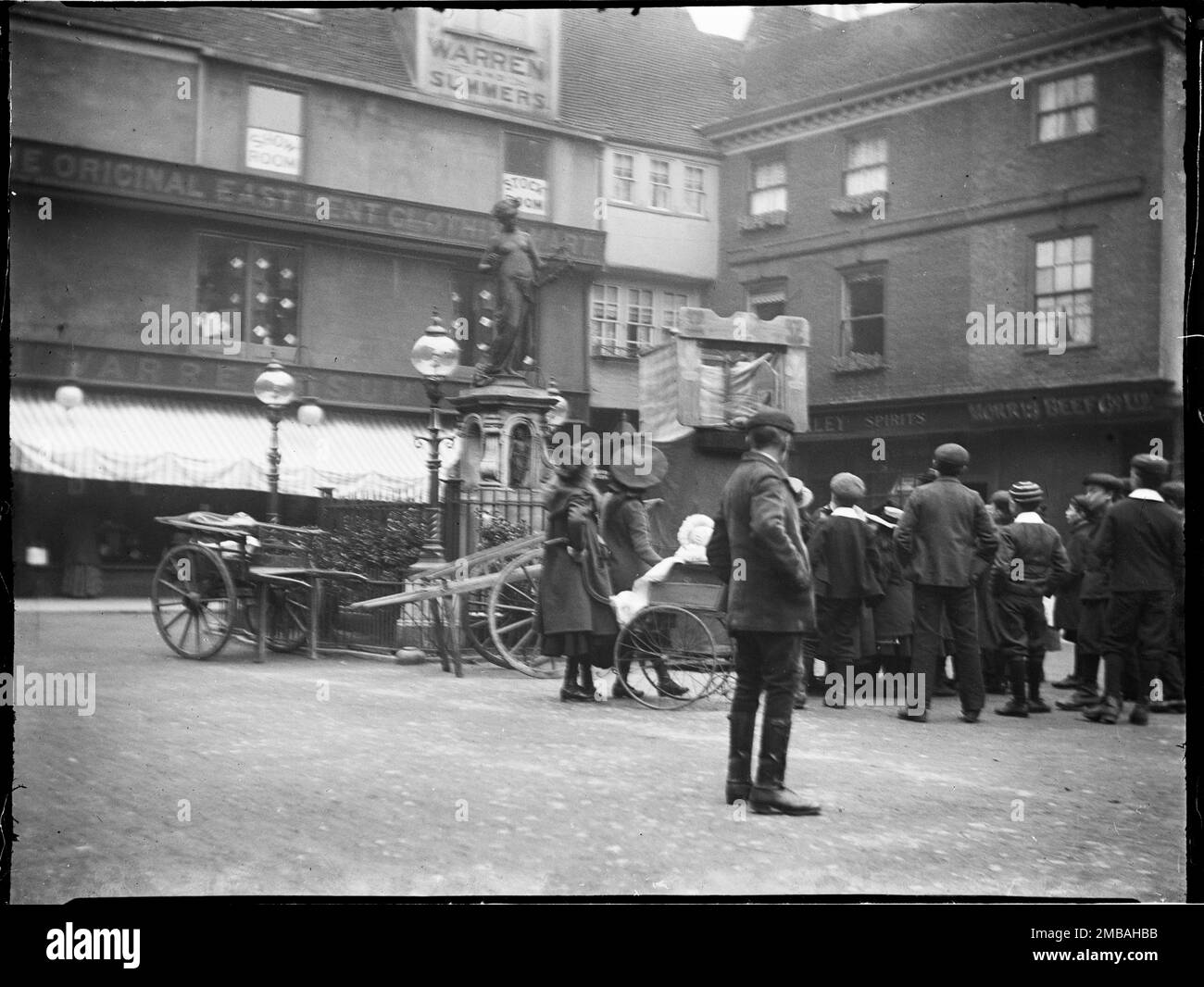 Marlowe Memorial, Buttermarket, Canterbury, Kent, 1904. Eine Gruppe von Kindern versammelte sich um einen Punch und Judy Stand neben dem Marlowe Memorial im Buttermarket. Das Marlowe Memorial ist eine Gedenkstätte für den Dichter Christopher Marlowe, die 1891 enthüllt wurde. 1993 wurde es außerhalb des Marlowe-Theaters verlegt. Stockfoto