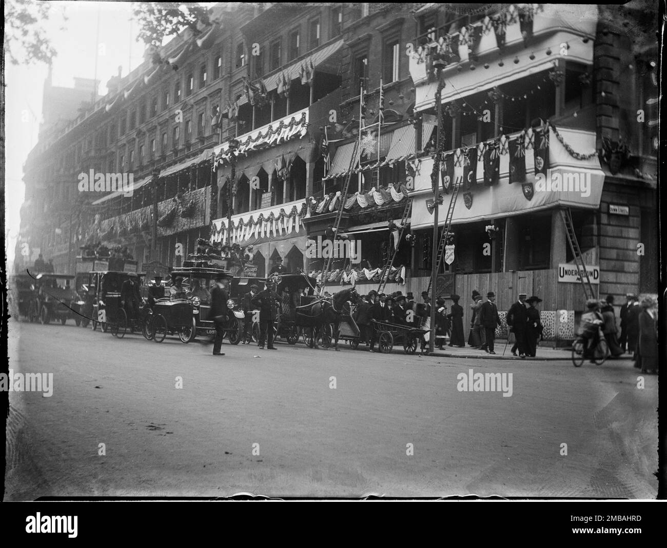 Piccadilly, City of Westminster, Greater London Authority, 1911. Ein Blick nach Westen entlang Piccadilly zeigt Verkehr, Fußgänger und einen Polizisten und Männer auf Leitern, die an der Vorderseite der Gebäude Krönungsdekorationen anbringen. Die Krönungsdekoration in London. An der Vorderseite der Gebäude für die Krönung von König George V. und Königin Mary am 22. Juni 1911 befinden sich Flaggen und Fähnchen. Stockfoto