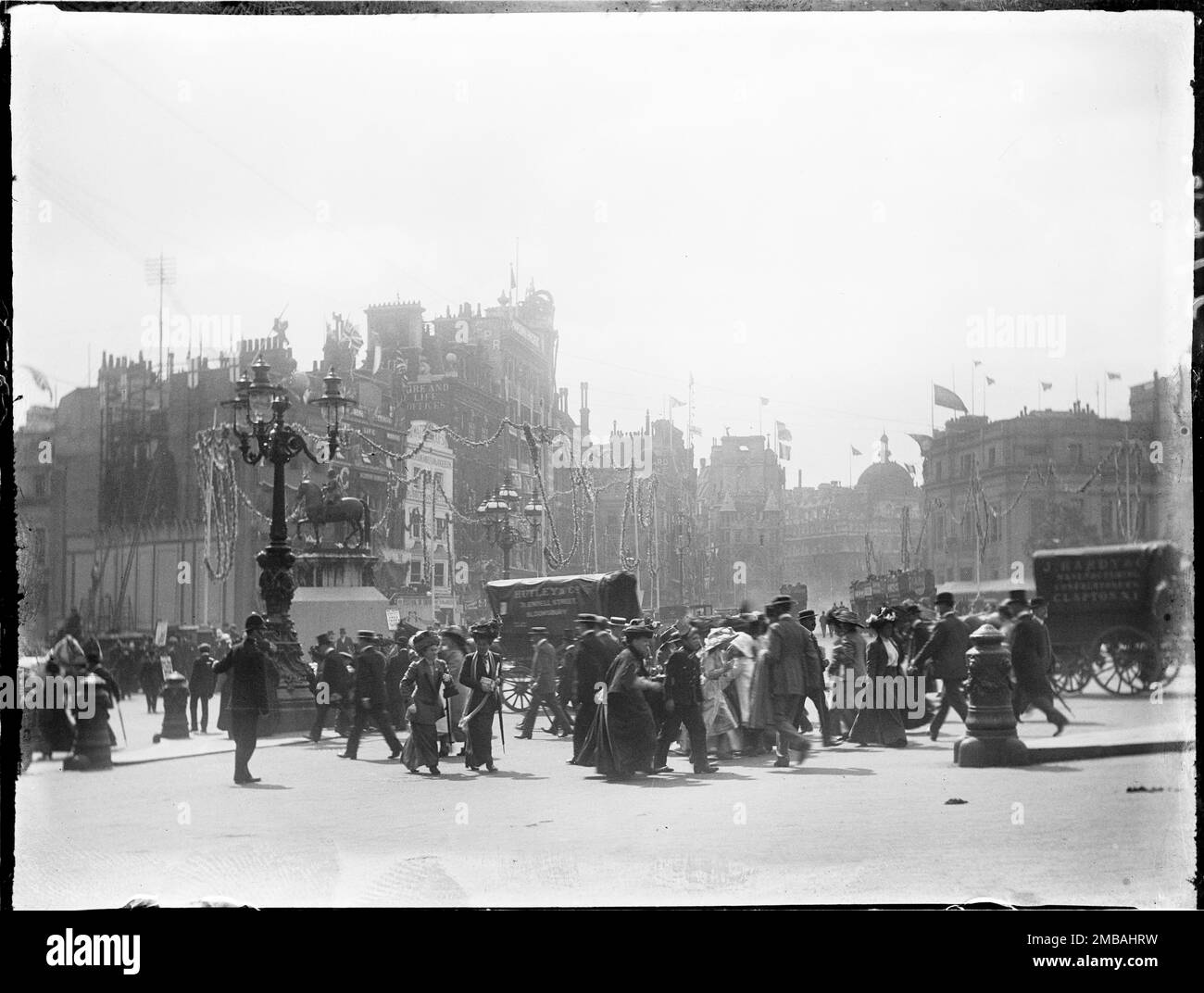 Charing Cross, City of Westminster, Greater London Authority, 1911. Eine belebte Straßenszene am Charing Cross, in der ein Polizist Fußgänger beim Überqueren der Straße zum und vom Trafalgar Square führt. Das Foto ist eines der Fotos, die der Fotograf aufgenommen hat, um die Krönungsdekorationen in London zu zeigen. Flaggen und Flöße schmücken die Umgebung für die Krönung von König George V. und Königin Mary am 22. Juni 1911. Stockfoto