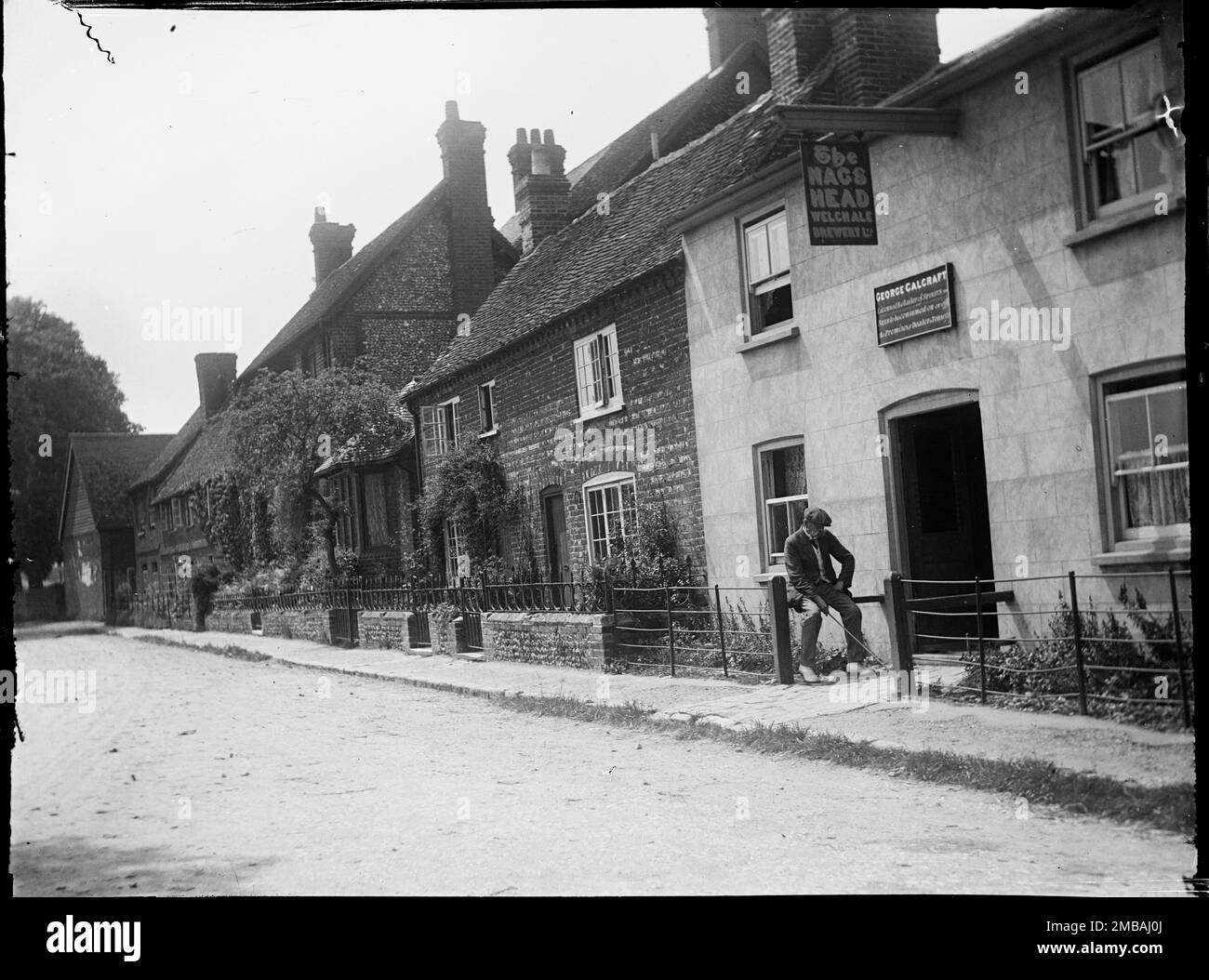 Aylesbury Road, Mönche Risborough, Princes Risborough, Wycombe, Buckinghamshire, 1918. Blick nach Süden entlang der Aylesbury Road in Monks Risborough, wobei ein Mann im Vordergrund vor dem Haus von Nag's Head mit Häusern dahinter sitzt. Seit dieses Foto aufgenommen wurde, ist der Pub geschlossen und wird jetzt als Haus genutzt. Ein Schild über der Tür zeigt, dass der Vermieter George Calcraft war und das Pub-Schild zeigt, dass der Pub Welch Ale Brewery Ltd. Gehört Stockfoto